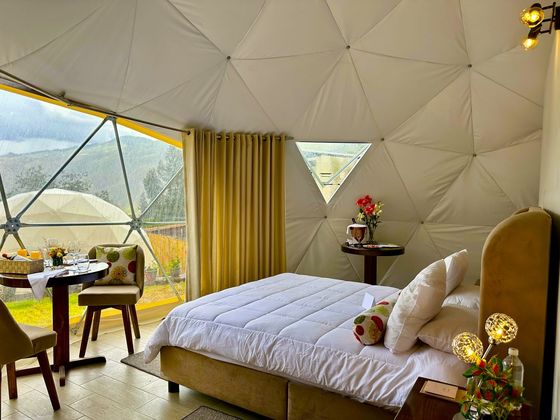 Interior del domo con cama, mesa para dos y vista a las montañas