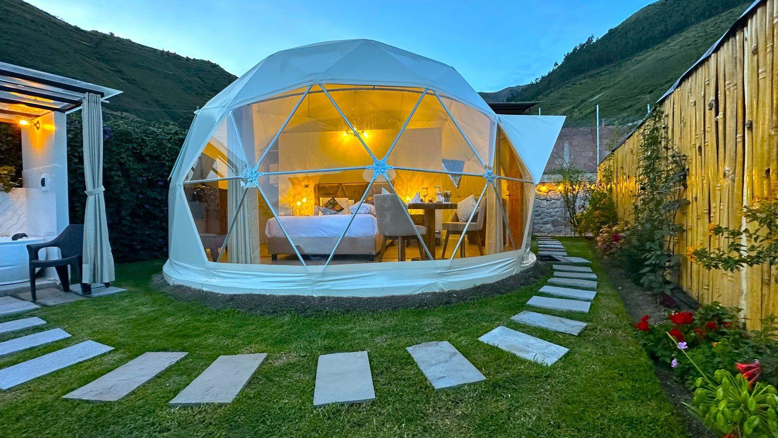 Domo geodésico iluminado al atardecer con jacuzzi y vista a las montañas del Valle Sagrado